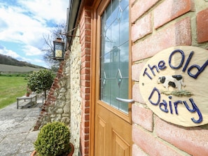 A brick building with a wooden door, a window with a glass pane, and a sign that reads 'The Old Dairy.'