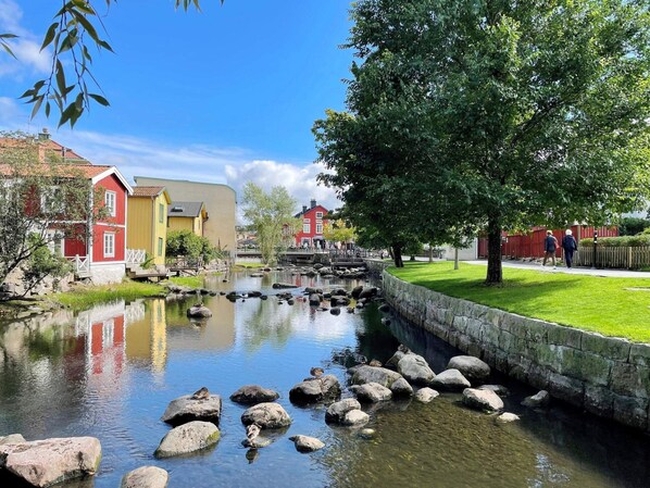 A calm river with rocks, a bridge, and buildings with red and yellow facades.