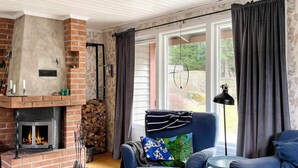 Un salon chaleureux avec une cheminée, un canapé bleu, une petite table et une grande fenêtre avec des rideaux.
