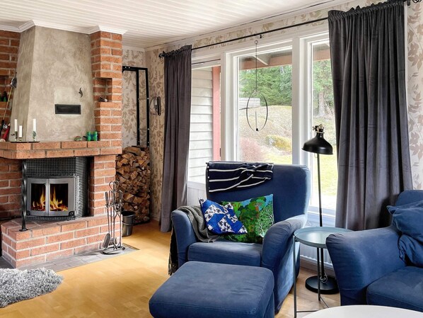 Uma sala de estar acolhedora com lareira, um sofá azul, uma mesa pequena e uma janela grande com cortinas.