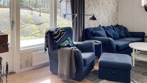 Une pièce avec un canapé bleu, un fauteuil, une petite table et une grande fenêtre avec des rideaux.