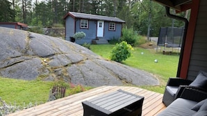Une terrasse en bois avec des meubles d’extérieur, une petite maison en arrière-plan et un grand rocher.