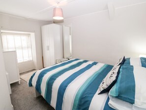 A bedroom with a bed, a wardrobe, a window, and a hanging light fixture.
