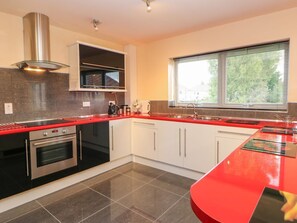 A modern kitchen with a red countertop, stainless steel appliances, white cabinets, and a window with blinds. - Mead House, Darlington (Darlington)