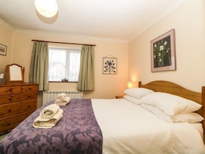 A bedroom with a bed, a dresser, a window with curtains, a wall-mounted picture, and a bedside lamp.