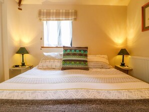 Un lit avec une literie à motifs, deux lampes de chevet, une fenêtre avec un rideau et un radiateur.