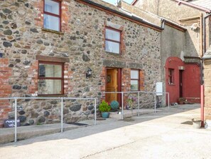 A stone building with a wooden door, a red door, and a metal railing in front.