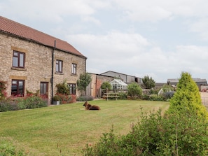 A stone building with a red-tiled roof, a green lawn, and a dog.