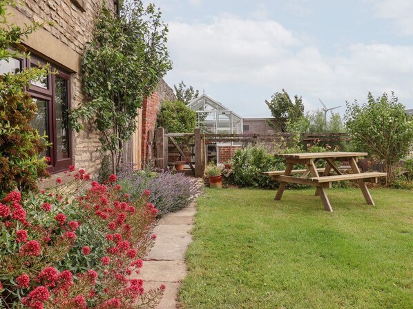 A garden with a wooden bench, a greenhouse, and a brick building.