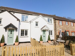 Une rangée de maisons à deux étages, aux façades blanches, aux portes vertes et surmontée d’une clôture en bois au premier plan.