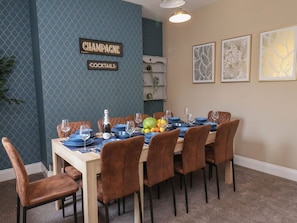 A dining area with a table set for six, blue plates, wine glasses, and a bottle.