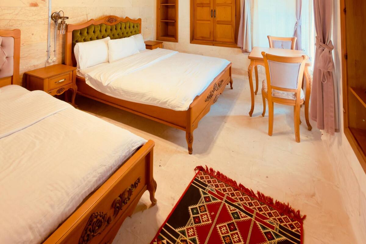 Un dormitorio con dos camas, muebles de madera, una pared de piedra y una ventana con cortinas.
