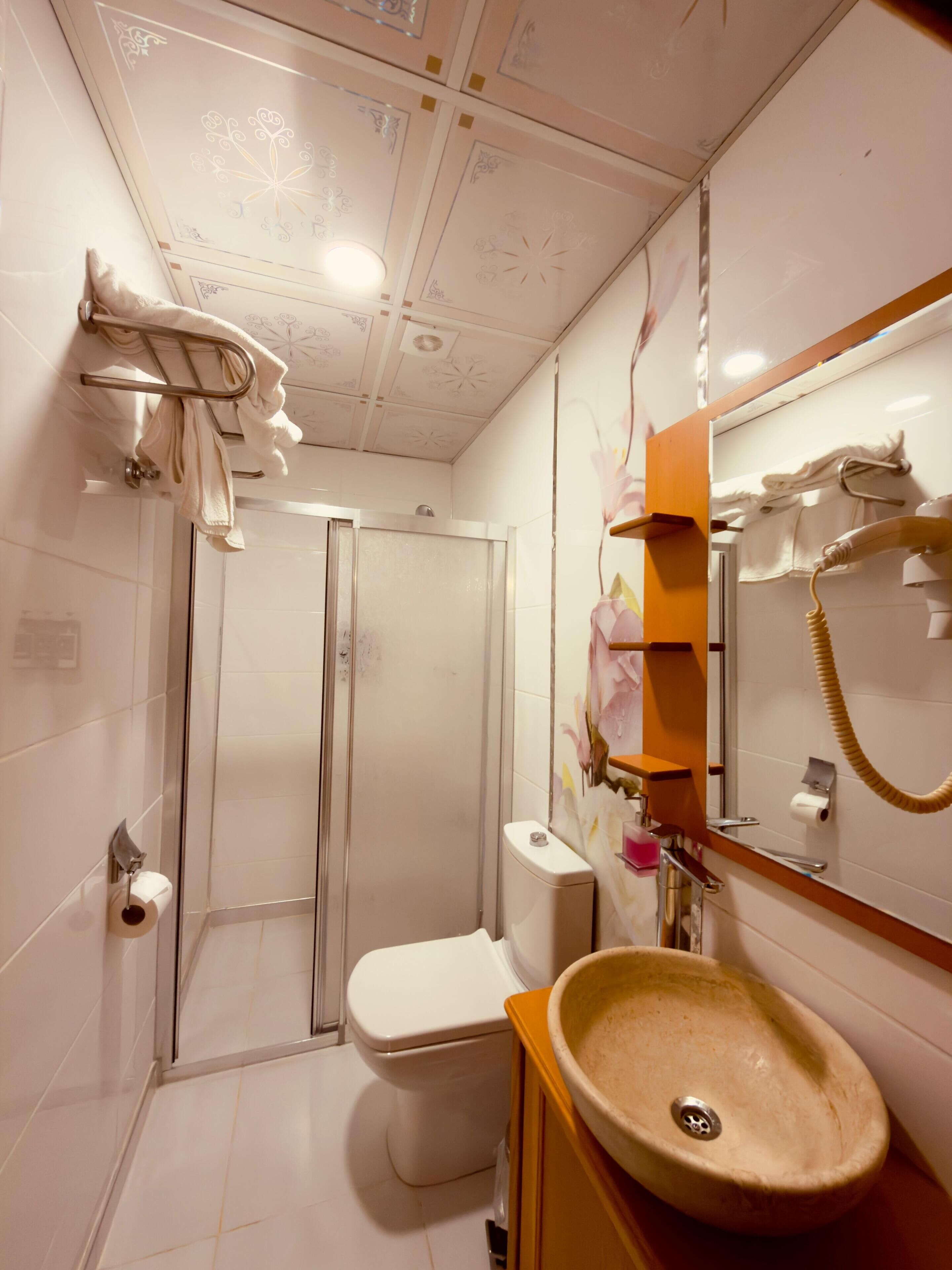 Un baño con cabina de ducha de vidrio, inodoro, lavabo y espejo con teléfono.