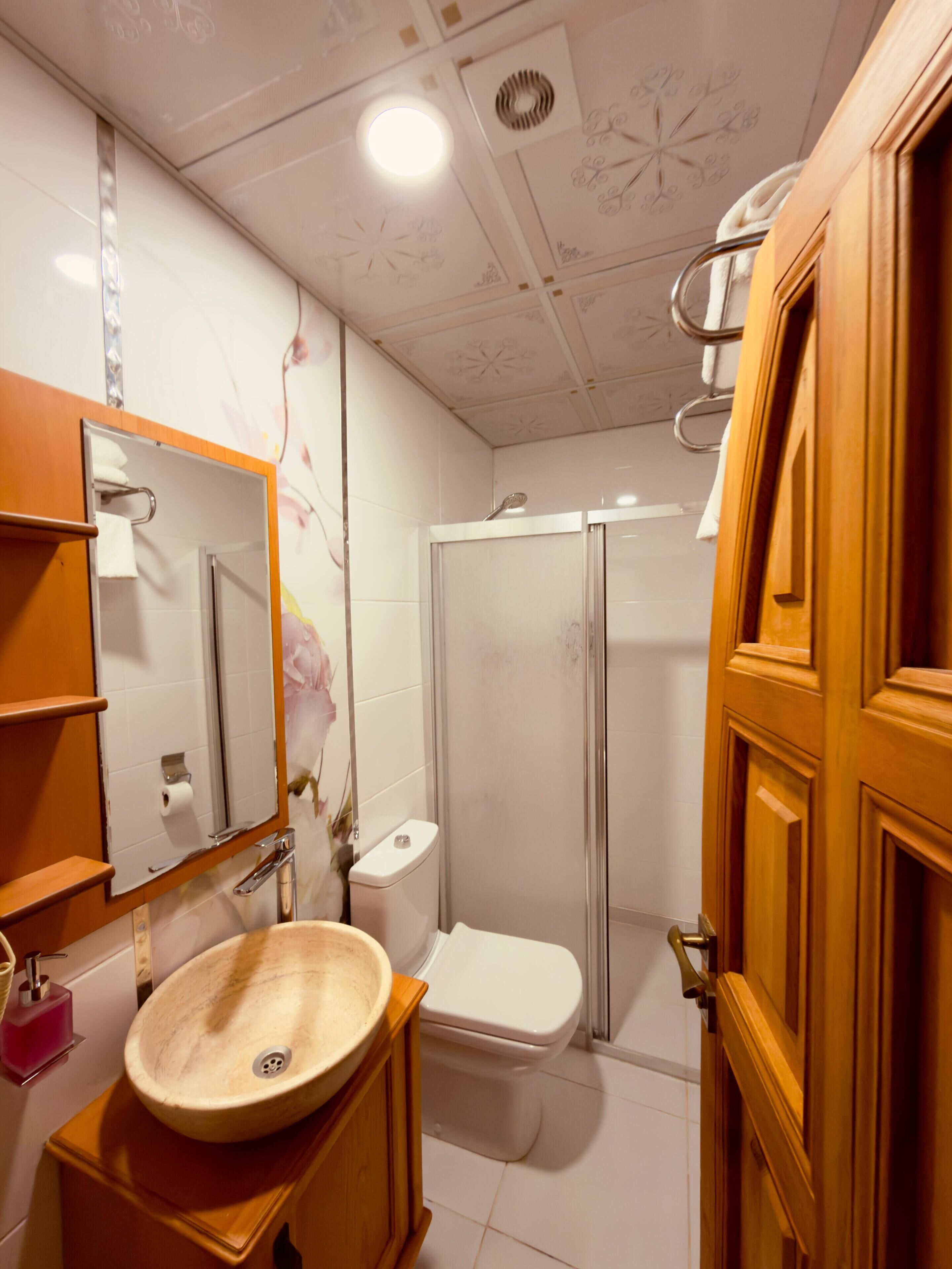 Un baño con tocador de madera, un lavabo redondo, un inodoro y una cabina de ducha.
