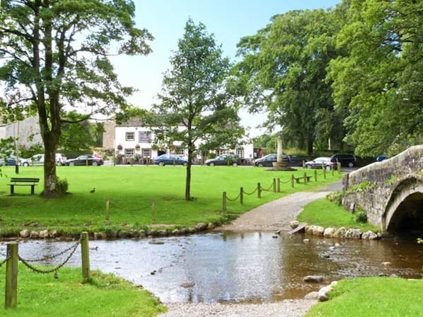 A park with a stream, a stone bridge, and a white building in the background.
