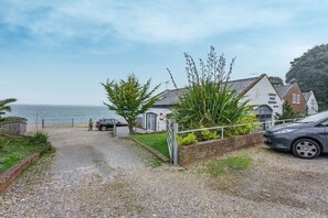 A coastal property with a gravel driveway, a parked car, and a building with a sign indicating holiday accommodation.