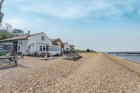 A coastal building with a patio area, outdoor seating, and a view of the sea.