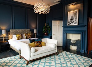 A bedroom with a bed, white sofa, patterned rug, and a fireplace.