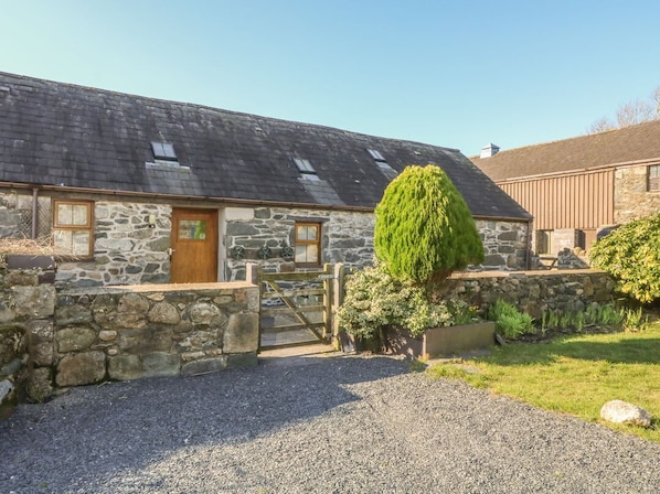 A stone building with a wooden door, a gravel driveway, and a well-maintained garden. - Beudy Bach, Y Felinheli (Caernarfon)