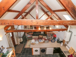 A loft-style room with exposed wooden beams, a central seating area, a washing machine, and a kitchen area with a sink and stove. - Beudy Bach, Y Felinheli (Caernarfon)