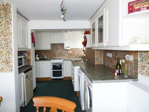 Una cocina compacta con armarios blancos, microondas, tostadora y lavadora.