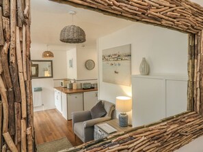 Un salon chaleureux avec une structure en bois rustique, un luminaire en fibres tressées, un tableau représentant un paysage côtier et une lampe sur une table d’appoint.