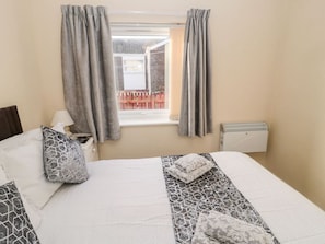 A hotel room with a bed, a window with curtains, a radiator, and a view of a red fence outside. - Primrose Cottage, Beadnell (Chathill)