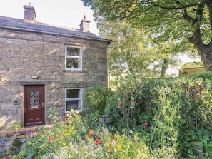 A stone house with a garden in front, a wooden door, and a window. - Sycamore Cottage, Hawes (Sedbergh)