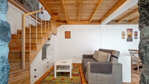 A cozy living area with a wooden staircase, a gray sofa, a white coffee table, and a patterned rug. - N T House by Homie in Porto Moniz (Porto Moniz)