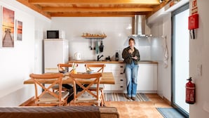 A kitchen with wooden beams, white cabinets, a dining table with chairs, a microwave, and a fire extinguisher. - N T House by Homie in Porto Moniz (Porto Moniz)