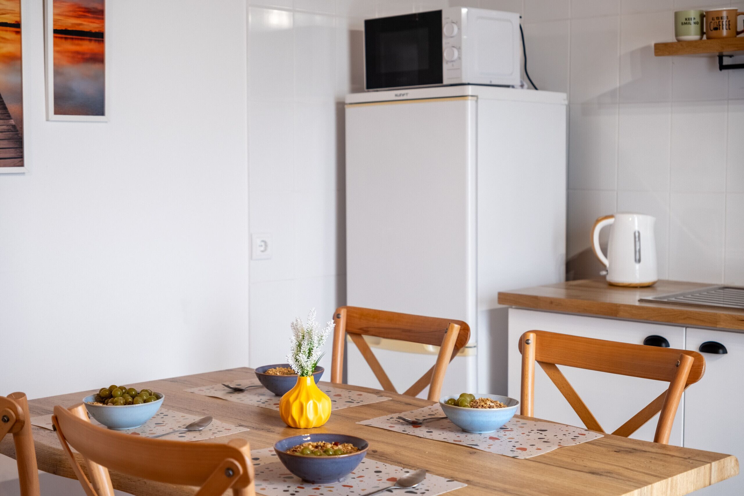 A kitchen with white cabinets, a microwave, a kettle, and a wooden table with chairs.