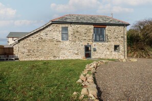 A stone building with a sloped roof, a small balcony, and a gravel driveway.