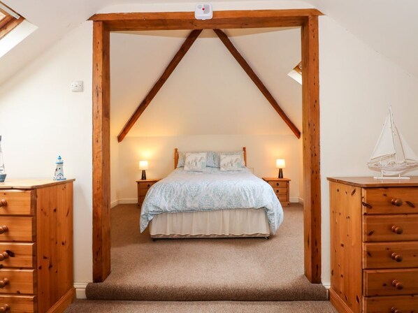 A bedroom with a sloped ceiling, wooden furniture, a bed with a light blue bedspread, bedside lamps, and a sailboat decoration.