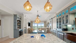 Een moderne keuken met een groot eiland, hanglampen en uitzicht naar buiten.