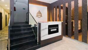 A reception desk labeled 'TOWNHOUSE' with a marble top, a staircase leading to an upper floor, and a fire exit sign. - Townhouse Birsa Railway Stadium Ranchi (Ranchi)