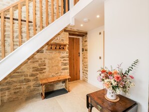 Una escalera con paredes de piedra, un banco de madera y un florero con flores sobre una mesa.
