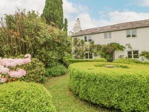 Un jardín bien cuidado con setos, plantas en flor y un edificio blanco con múltiples ventanas.