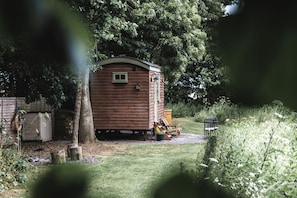 Una petita cabana de fusta amb un porxo, envoltada d'arbres i una zona verda.