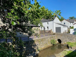 A stone bridge over a small stream, a white building with a grey roof, and a wooden fence.