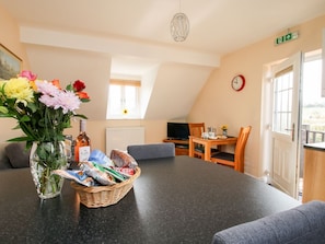 A dining area with a table, chairs, a vase of flowers, a basket of snacks, and a clock on the wall.