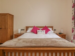 Un dormitorio con una cama de madera, dos mesitas de noche, un armario de madera y una cortina con estampado floral.