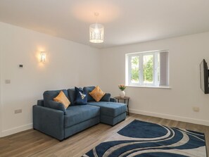 A modern living room with a sectional sofa, a patterned rug, a small side table, and a window with blinds.