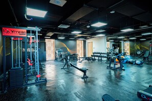 A gym with various exercise equipment, a sign that reads 'Olympia achieve your fitness', and a patterned wall design. - Tulip Residences Muscat The Village (Seeb)