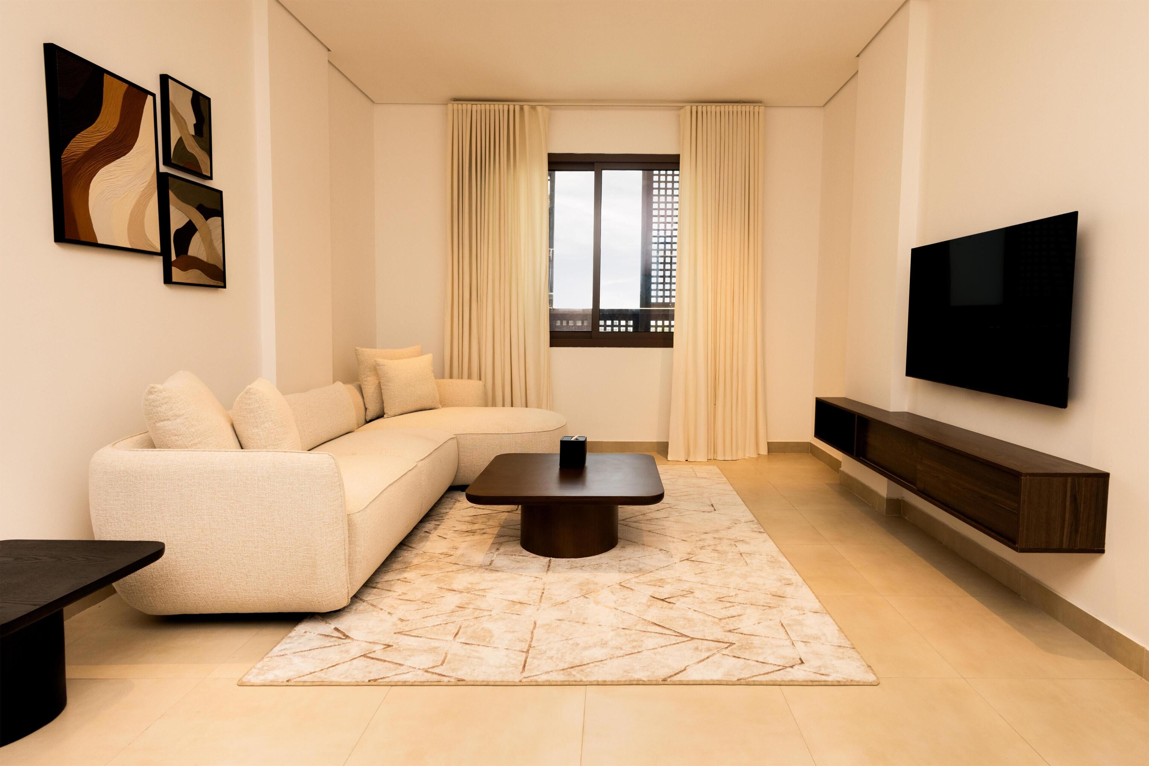 A modern living room with a sectional sofa, a coffee table, a flat-screen TV, and artwork on the walls.