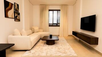 A modern living room with a sectional sofa, a coffee table, a flat-screen TV, and artwork on the walls.