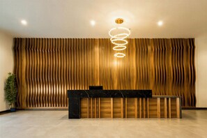A reception area with a wooden slatted wall, a reception desk, and a modern light fixture. - Tulip Residences Muscat The Village (Seeb)