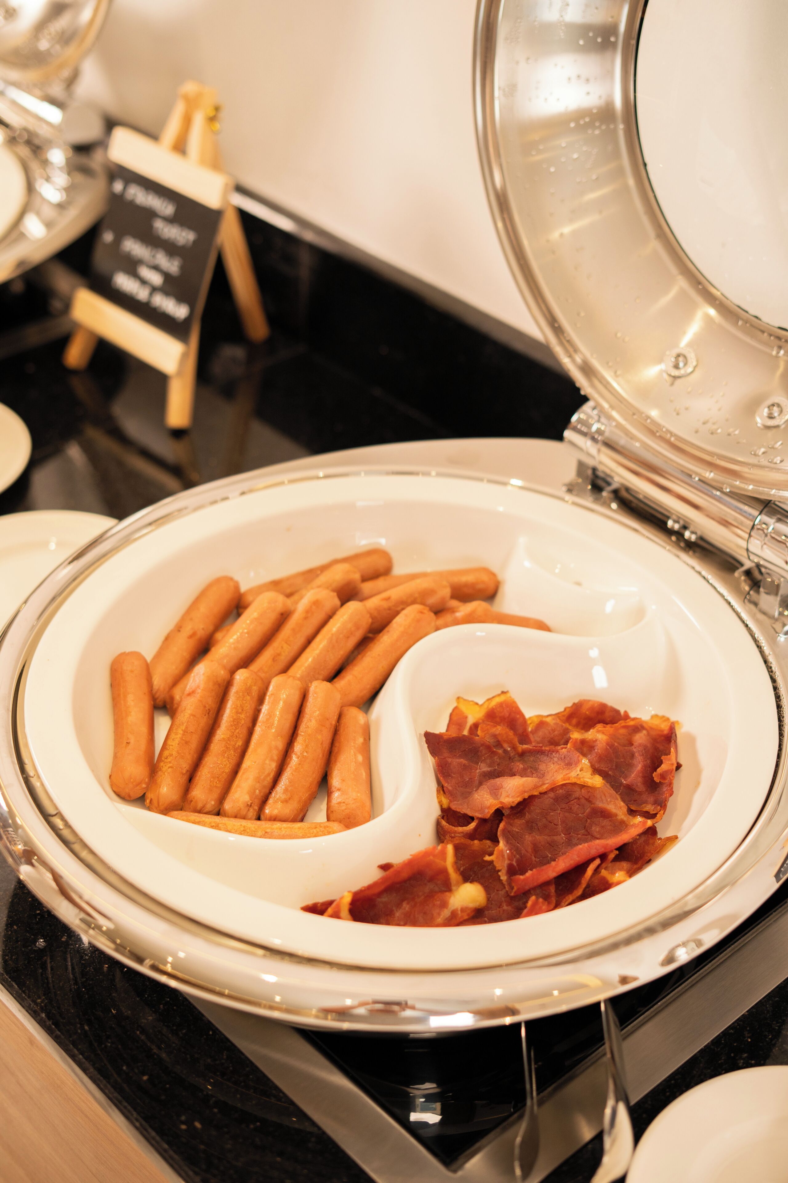 Un bufé con un bol de salchichas y un recipiente pequeño de tocino.