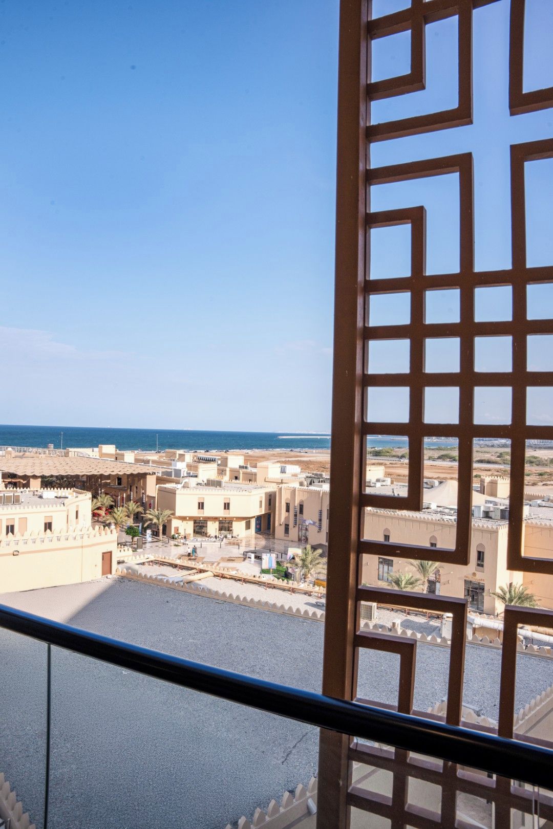 A view through a window with a geometric pattern, overlooking a coastal area with buildings and a clear sky.