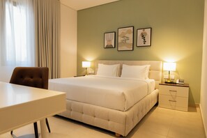 A hotel room with a bed, bedside tables, a desk, and a chair. There are three framed artworks on the wall. - Tulip Residences Muscat The Village (Seeb)
