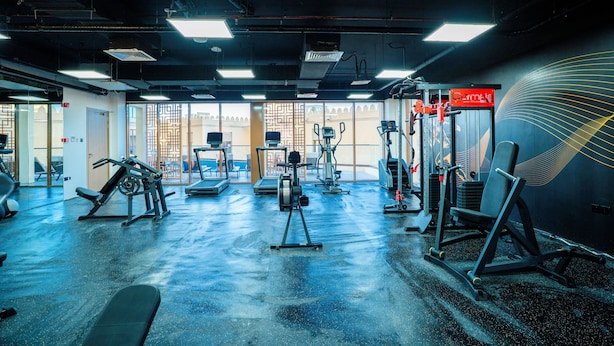 A gym with various exercise equipment, a wall with a geometric design, and a door leading outside.